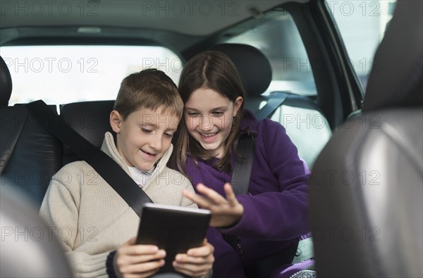 Boy and girl (8-9, 10-11) using digital tablet in car.