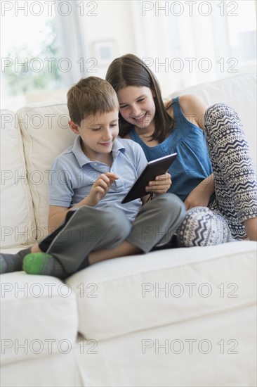 Boy and girl (8-9, 10-11) sitting on sofa using digital tablet.