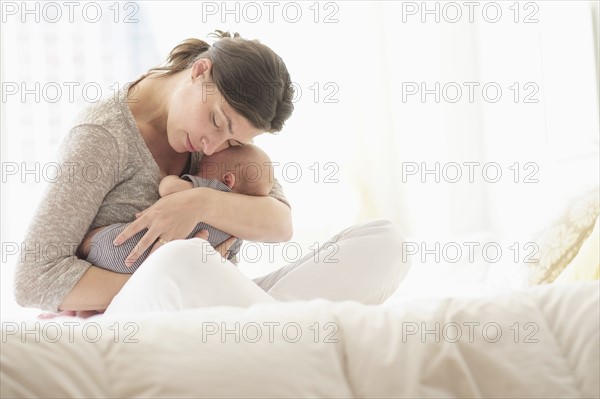 Mother embracing baby boy (2-5 months) in bed.