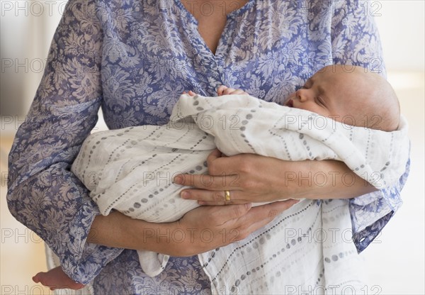 Close up of baby boy (2-5 months) sleeping in mother's arms.