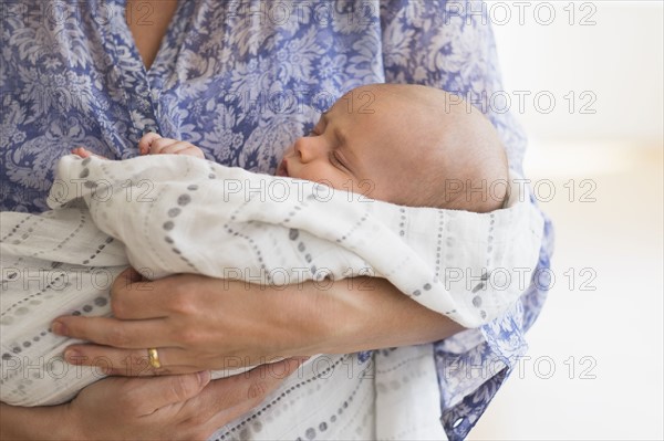 Close up of baby boy (2-5 months) sleeping in mother's arms.