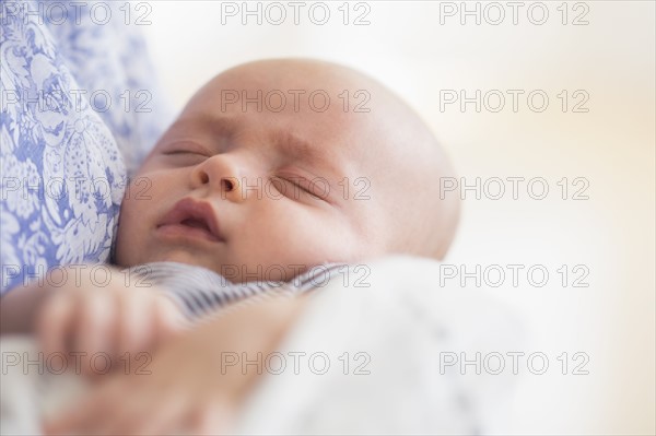 Close up of baby boy (2-5 months) sleeping in mother's arms.