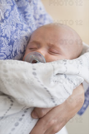 Close up of baby boy (2-5 months) sleeping in mother's arms.