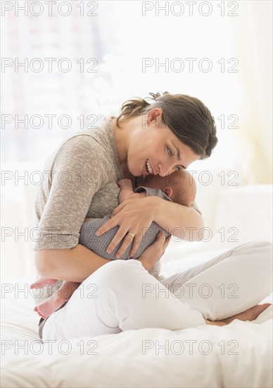 Mother embracing baby boy (2-5 months) in bed.