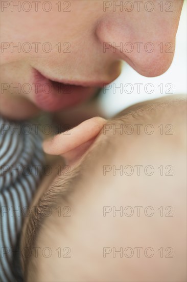 Close up of mother's mouth whispering into baby boy's(2-5 months) ear.