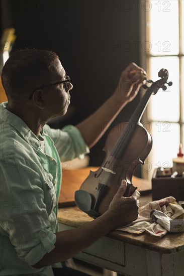 Mature man fixing violin in his workshop.