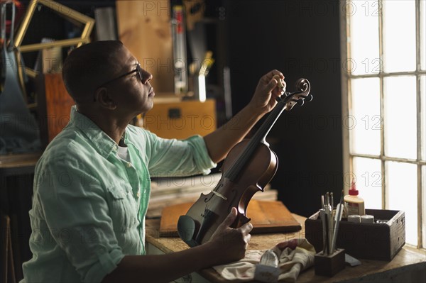 Mature man fixing violin in his workshop.