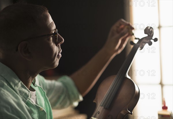 Mature man fixing violin in his workshop.