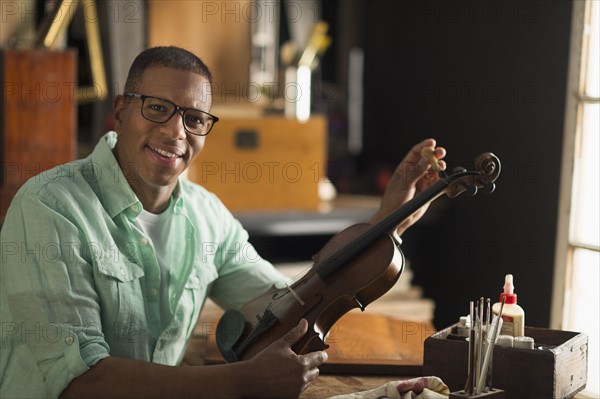 Portrait of mature man fixing violin in his workshop.