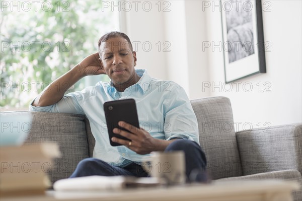 Man sitting on sofa at home and using digital tablet.