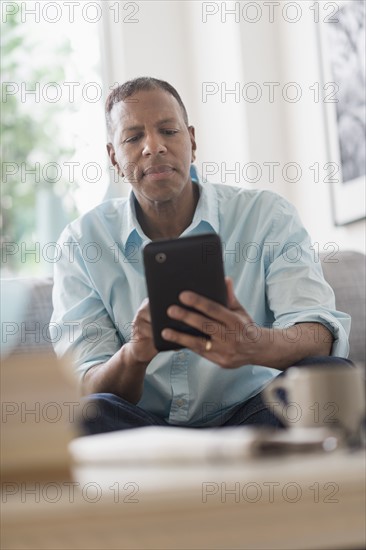 Man sitting on sofa at home and using digital tablet.