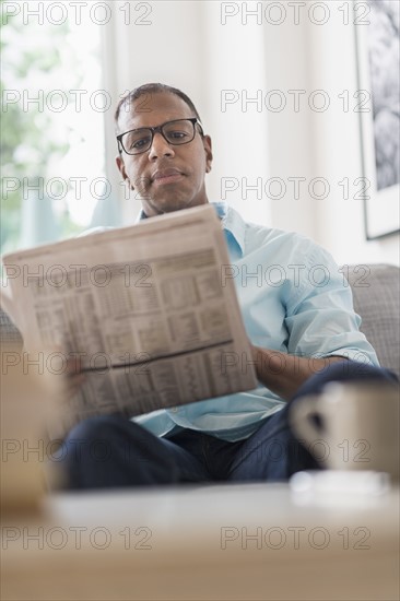 Man reading newspaper on sofa.