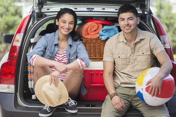 Portrait of young couple sitting in open car trunk.