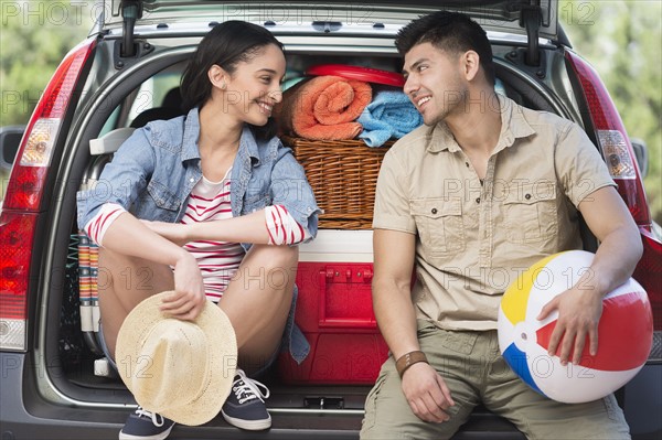 Young couple sitting in open car trunk.