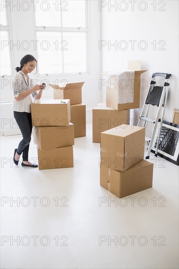 Young woman standing among boxes in new home and using mobile phone.