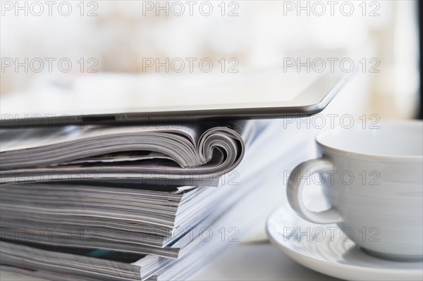 Close up of coffee cup and digital tablet on top of magazine stack.