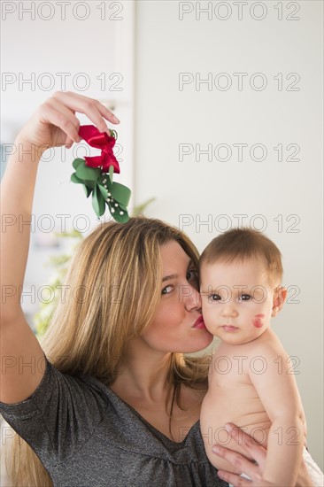 Mother holding baby girl (6-11 months) and mistletoe.
Photo : Jamie Grill