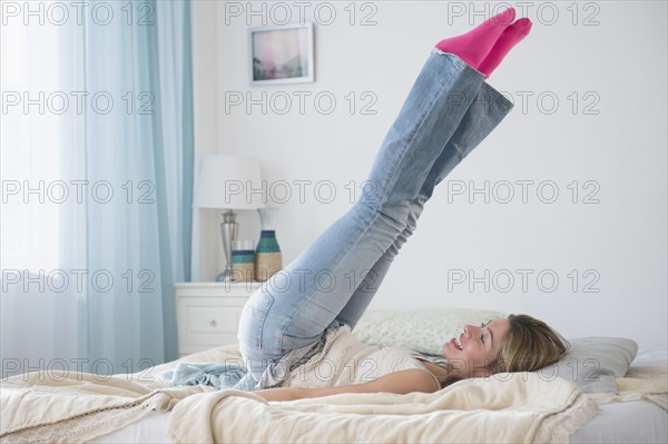 Young woman lying on bed with legs up.
Photo : Jamie Grill