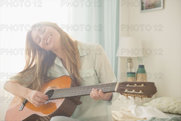 Young woman playing acustic guitar on bed.
Photo : Jamie Grill