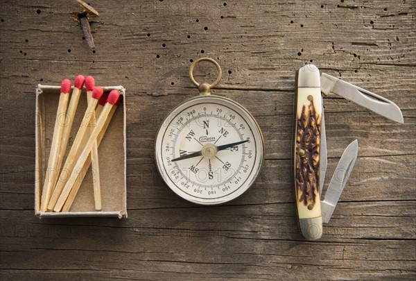 Studio Shot of matchsticks, compass and knife on wooden board.
Photo : Jamie Grill