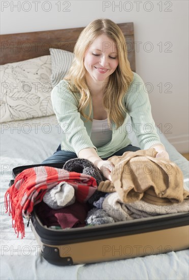 Woman sitting on bed and packing suitcase.
Photo : Jamie Grill