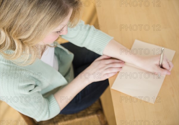 Blond woman sitting down and writting letter.
Photo : Jamie Grill