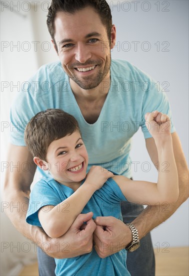 Father embracing son (8-9), Boy flexing muscles.
Photo : Jamie Grill