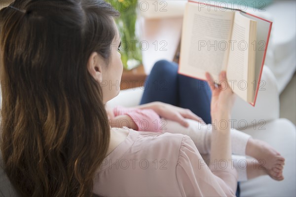Young woman reading book and holding daughter(6-11 months).
Photo : Jamie Grill