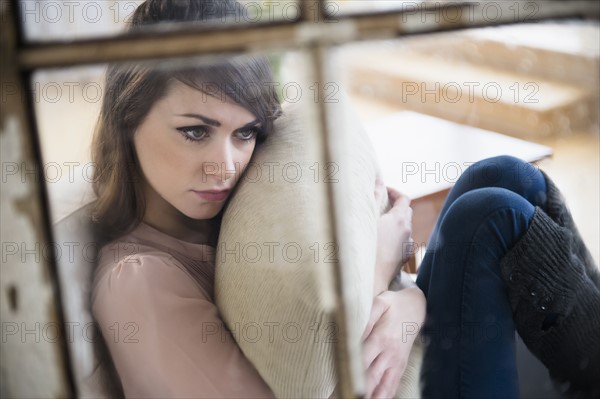 Young woman contemplating in living room with pillow in hands.
Photo : Jamie Grill