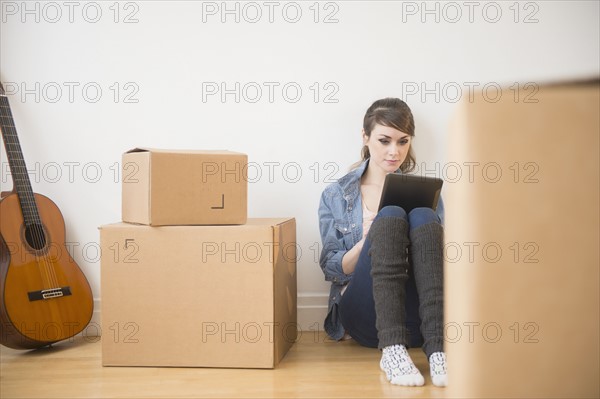 Young woman sitting on floor with digital tablet with boxes around her.
Photo : Jamie Grill