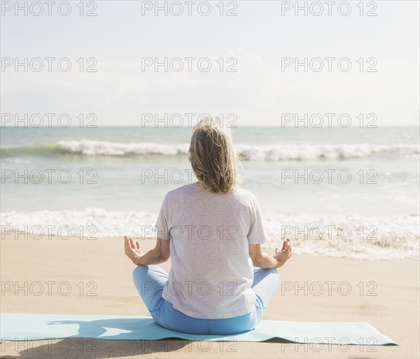 Senior woman practicing yoga on beach.
Photo : Daniel Grill