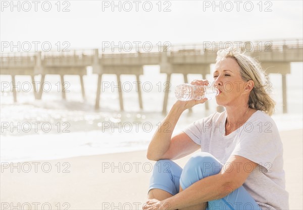 Senior woman drinking water on beach.
Photo : Daniel Grill