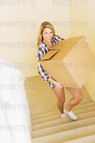 Young woman carrying box in her new house.
Photo : Daniel Grill