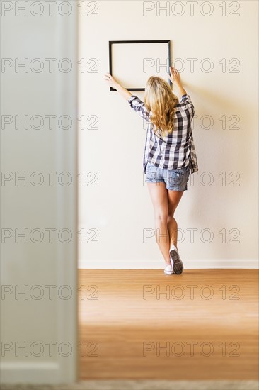 Rear view of woman hanging picture frame on wall.
Photo : Daniel Grill