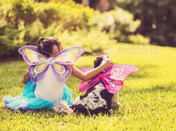 Rear view of girl (8-9) wearing fairy costume stroking dog.
Photo : Daniel Grill