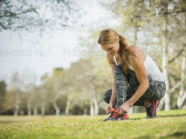 Woman in park tying shoe.