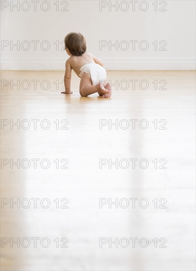 Rear view of baby girl (18-23 months) on hardwood floor.