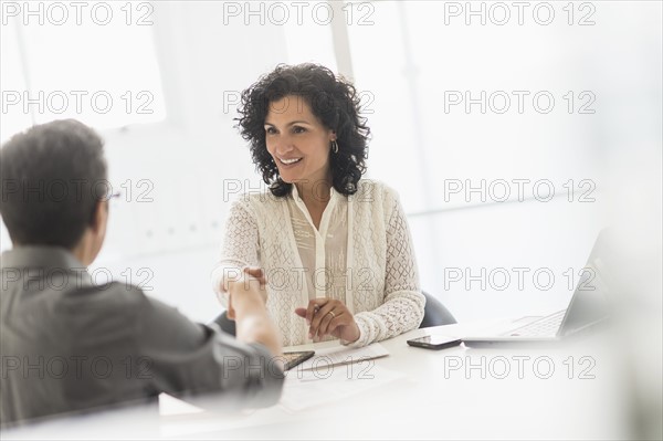 Business people shaking hands at desk in office.