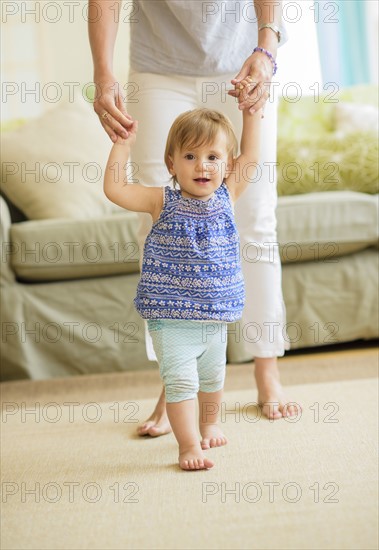 Mother assisting baby daughter (18-23 months) with her first steps.