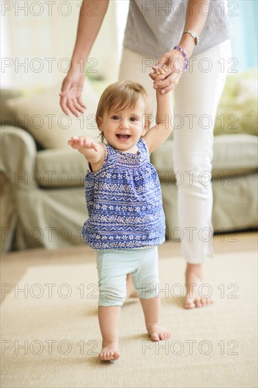 Mother assisting baby daughter (18-23 months) with her first steps.