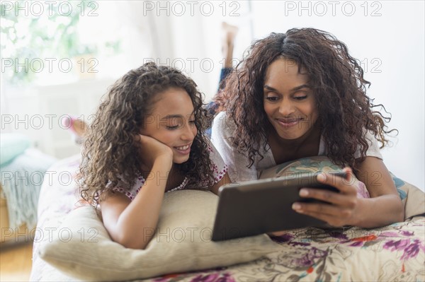 Mother with daughter (8-9) using digital tablet on bed.