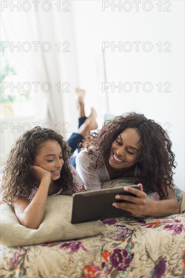 Mother with daughter (8-9) using digital tablet on bed.