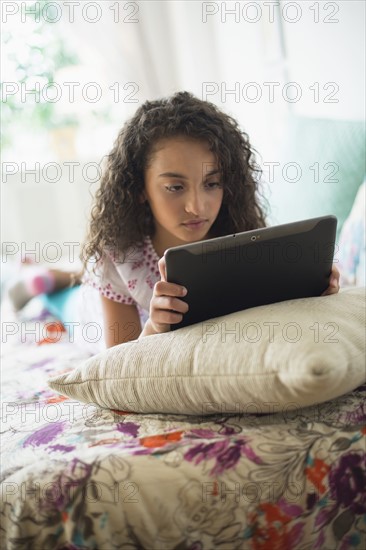 Girl (8-9) using digital tablet on bed.