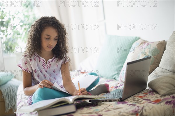 Girl (8-9) studying on bed.