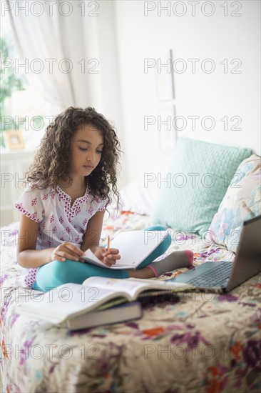 Girl (8-9) studying on bed.