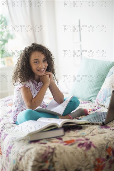 Girl (8-9) studying on bed.