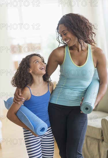 Mother and daughter (8-9) holding yoga mats in living room.