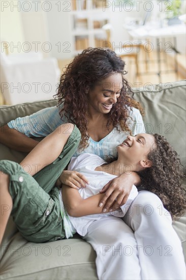 Mother tickling daughter (8-9) on sofa.