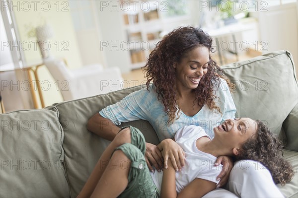 Mother tickling daughter (8-9) on sofa.