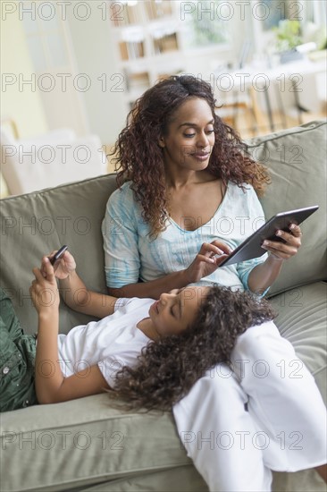 Mother and daughter (8-9) relaxing on sofa.